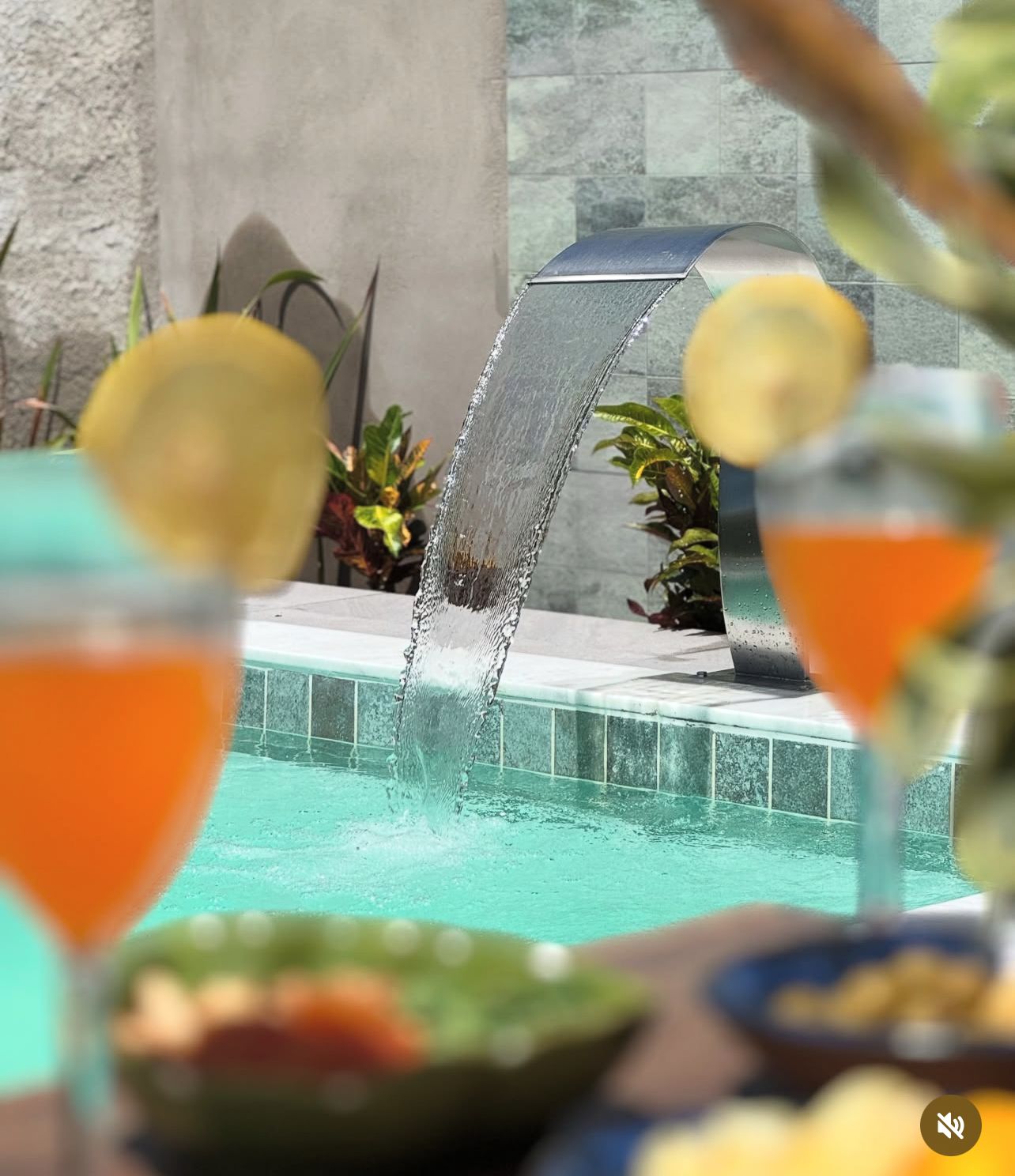 Detalhe de cascata curva em aço sobre piscina com drinks ao redor