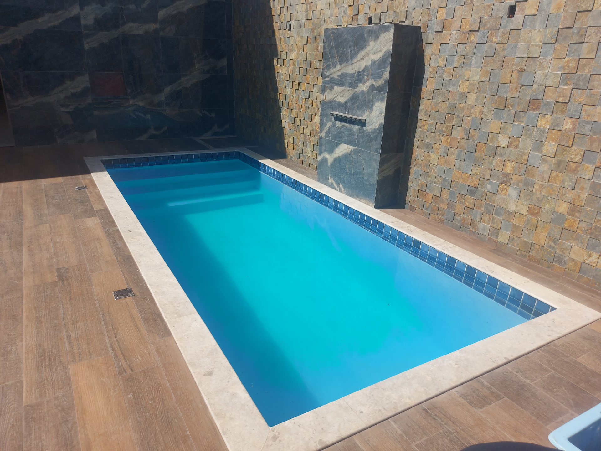 Piscina retangular interna com revestimento azul e parede de pedras
